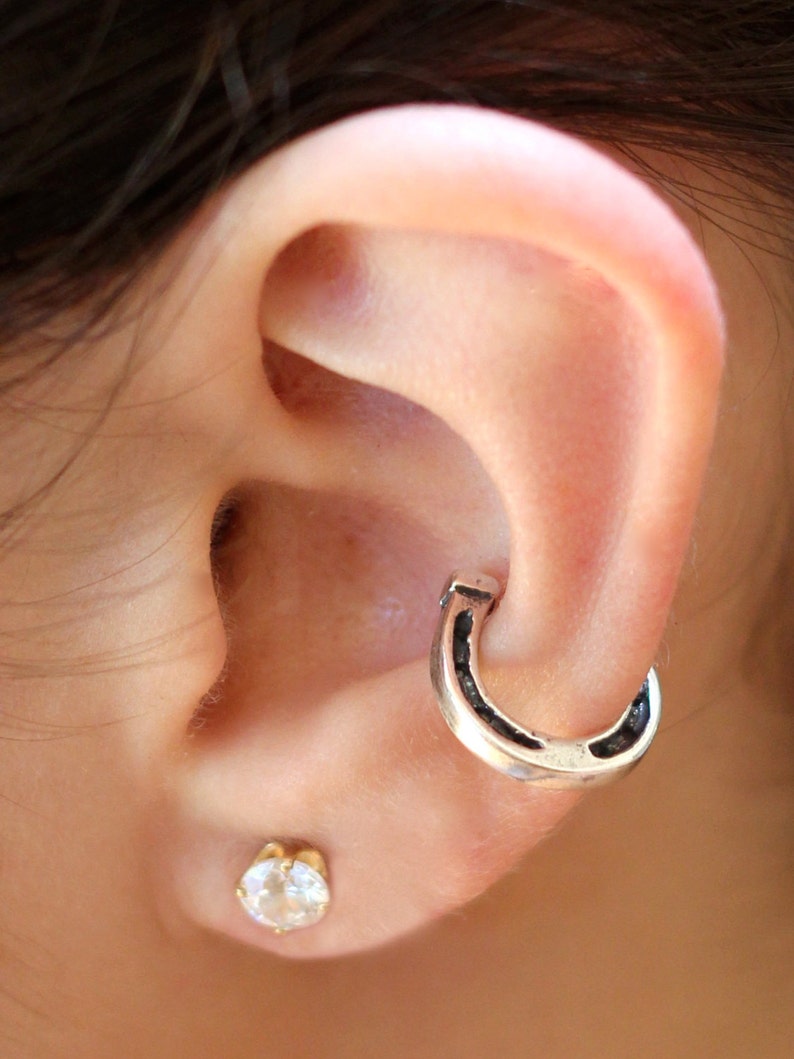May include: A close-up of a person's ear with a silver horseshoe hoop earring and a small clear gemstone stud earring.