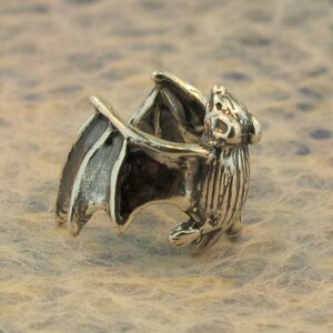 May include: A silver bat ring with detailed wings and a textured body. The ring is designed to be worn on the finger.