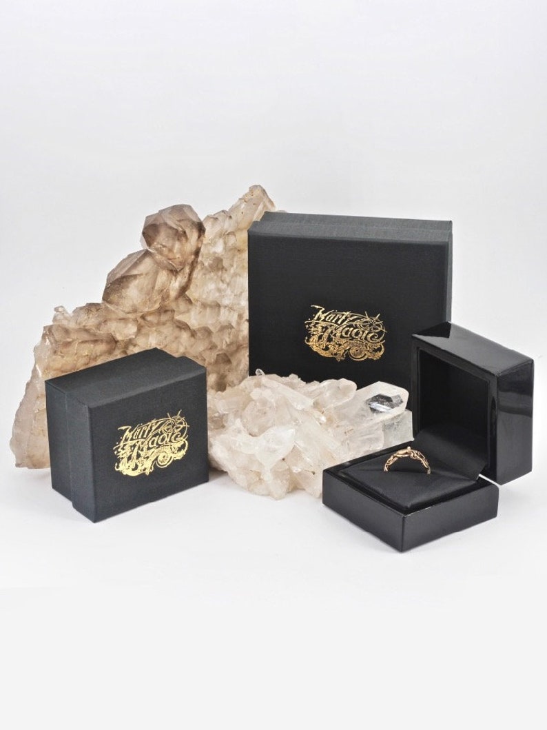 Op de afbeelding: Twee zwarte dozen met gouden letters die "Marty Magic" lezen en een kleinere zwarte doos met een gouden ring erin.