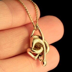 May include: A gold chain necklace with a pendant shaped like a knot. The pendant is made of a single piece of gold and is very detailed.