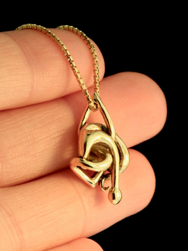 May include: A gold chain necklace with a pendant shaped like a knot. The pendant is made of a single piece of gold and is very detailed.