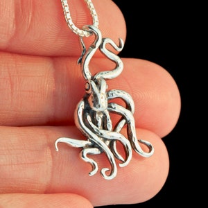 May include: A silver octopus pendant with a detailed, textured design hangs from a silver chain. The pendant is about 2 inches tall and is a popular choice for ocean-themed jewelry.