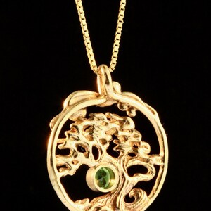 May include: A gold necklace with a pendant featuring a stylized tree with a green gemstone in the center.