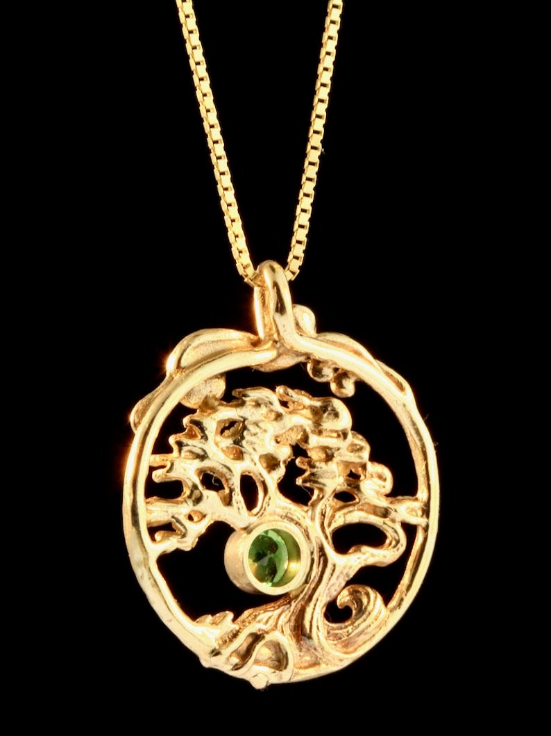 May include: A gold necklace with a pendant featuring a stylized tree with a green gemstone in the center.