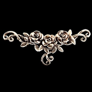 May include: A gold-toned metal rose vine design with three roses and leaves. The design is intricate and detailed.