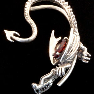 K&ouml;nnte beinhalten: Silberner Drachen-Ohrring mit einem roten Edelstein. Der Drachenschwanz umschlie&szlig;t das Ohr und der Kopf schaut nach vorne.