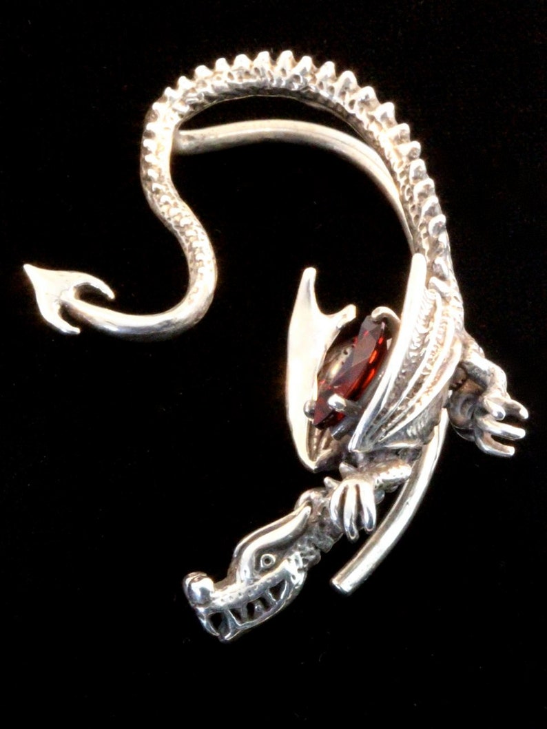K&ouml;nnte beinhalten: Silberner Drachen-Ohrring mit einem roten Edelstein. Der Drachenschwanz umschlie&szlig;t das Ohr und der Kopf schaut nach vorne.