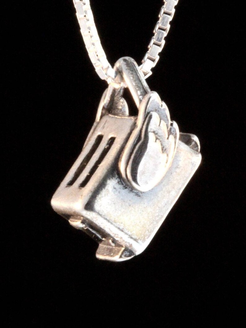May include: A silver charm necklace featuring a detailed miniature toaster with wings. The charm is attached to a silver chain.
