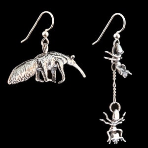 May include: A pair of silver earrings. The left earring features a detailed ant-eater charm. The right earring features a dangling charm with an ant and a spider.