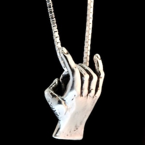 May include: A silver necklace with a hand pendant. The hand is making the 'okay' sign.