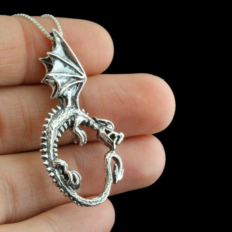 Op de afbeelding: Een zilveren drakenhangerketting met een gedetailleerd ontwerp. De draak is opgerold met zijn staart in zijn bek.