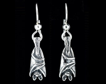 May include: A pair of silver dangle earrings featuring a detailed bat design. The bats are hanging upside down with their wings spread out.