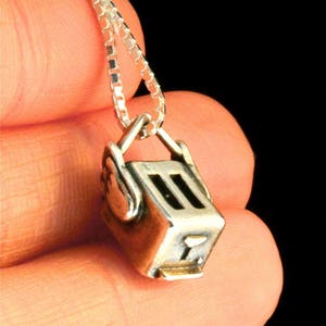 May include: A silver chain necklace with a silver charm in the shape of a toaster. The charm has a black detail on the front.
