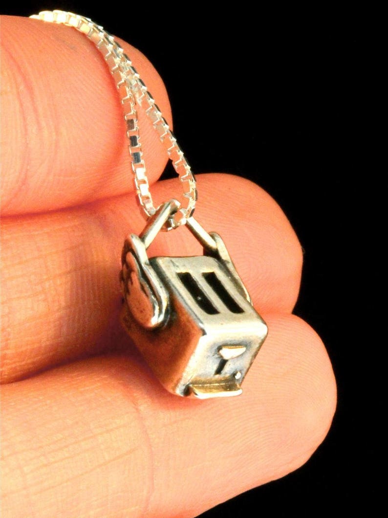 May include: A silver chain necklace with a silver charm in the shape of a toaster. The charm has a black detail on the front.