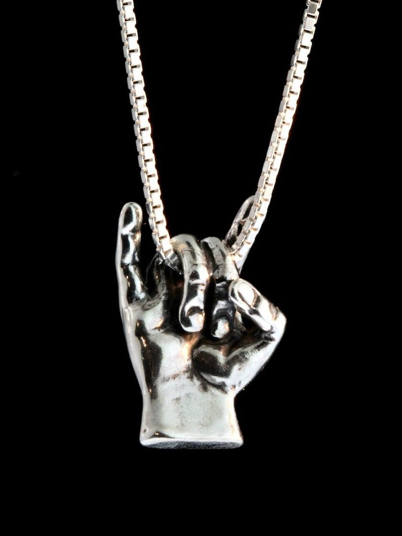 May include: A silver necklace with a pendant shaped like a hand making the 'I love you' sign in American Sign Language.