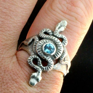 May include: A silver ring featuring a detailed snake design with a blue gemstone in the centre.