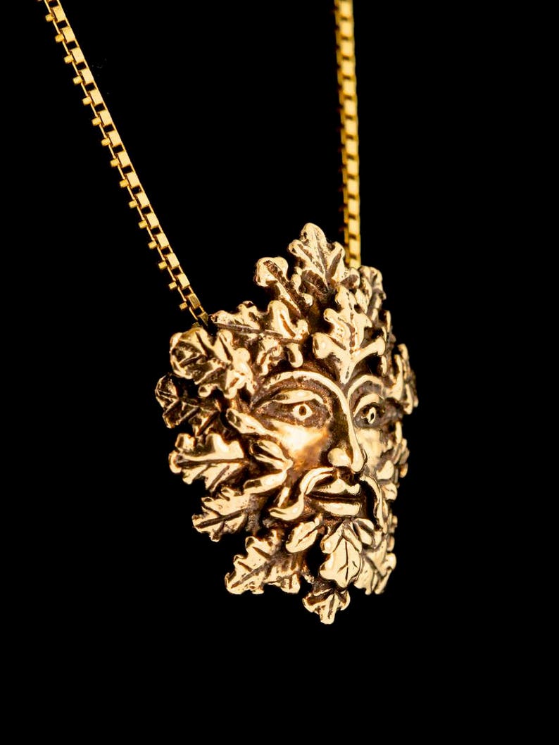 Pu&ograve; includere: Una collana d'oro con un ciondolo che presenta un designo dettagliato di Green Man. Il ciondolo &egrave; in metallo e ha un viso circondato da foglie e rami.