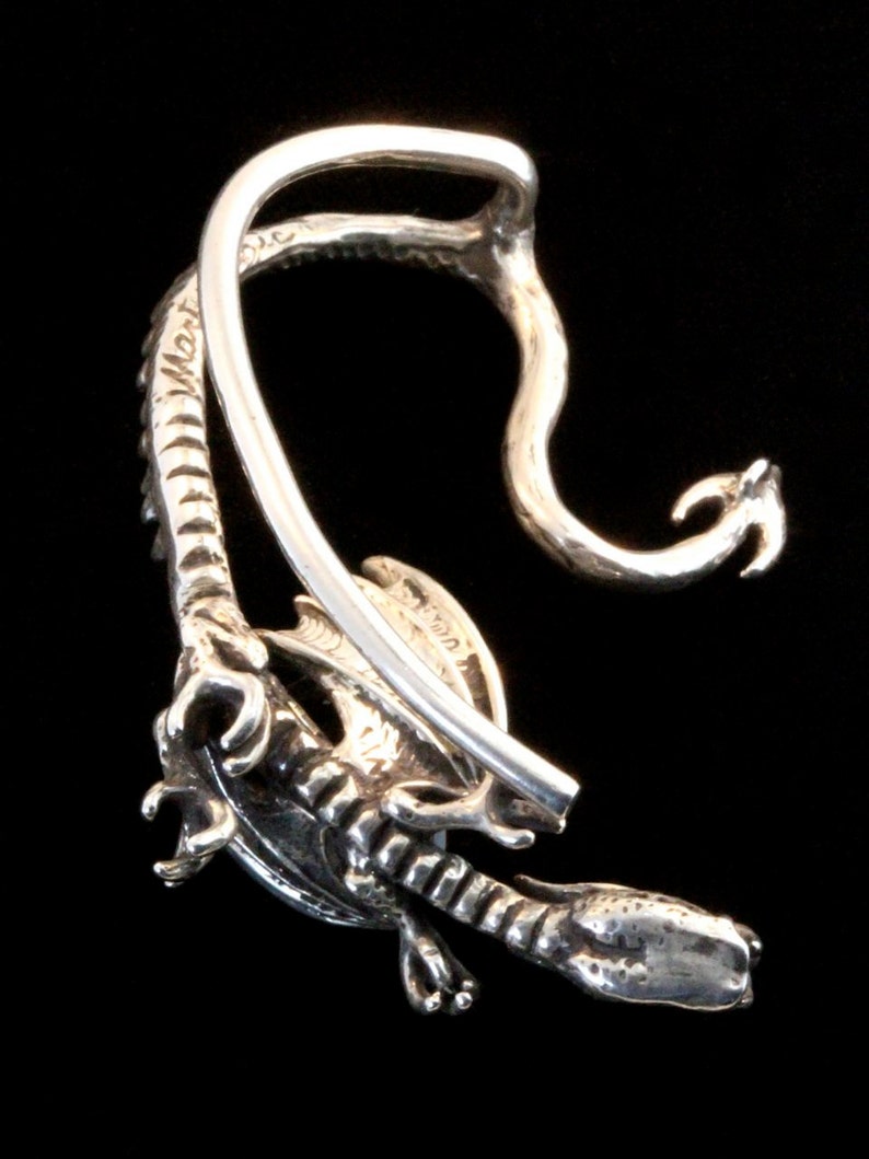 K&ouml;nnte beinhalten: Silberner Drachen-Ohrclip mit detailliertem Design. Der Clip ist offen und hat eine Drahtschlaufe zum Anbringen am Ohr.