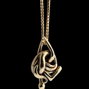 May include: A gold chain necklace with a pendant shaped like a stylized figure. The figure is abstract and appears to be in a contorted pose.