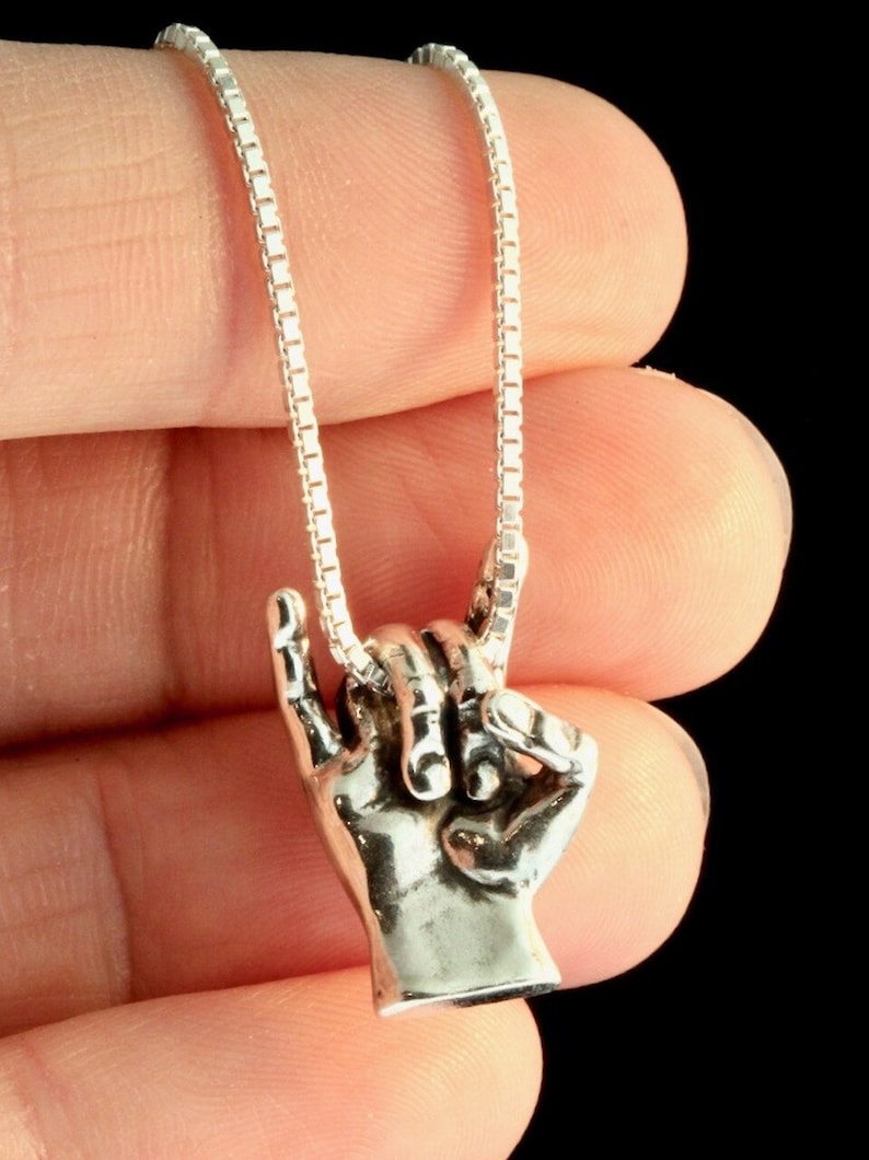 May include: A silver chain necklace with a pendant of two hands clasped together in a rock and roll hand gesture.