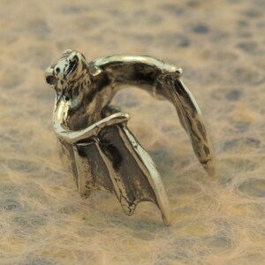 May include: A silver bat ring with wings spread out. The bat is facing forward with its mouth open.
