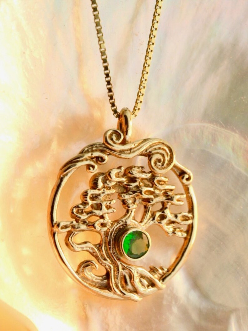 May include: Gold necklace with a tree of life pendant featuring a green gemstone. The pendant is round and has a detailed design.