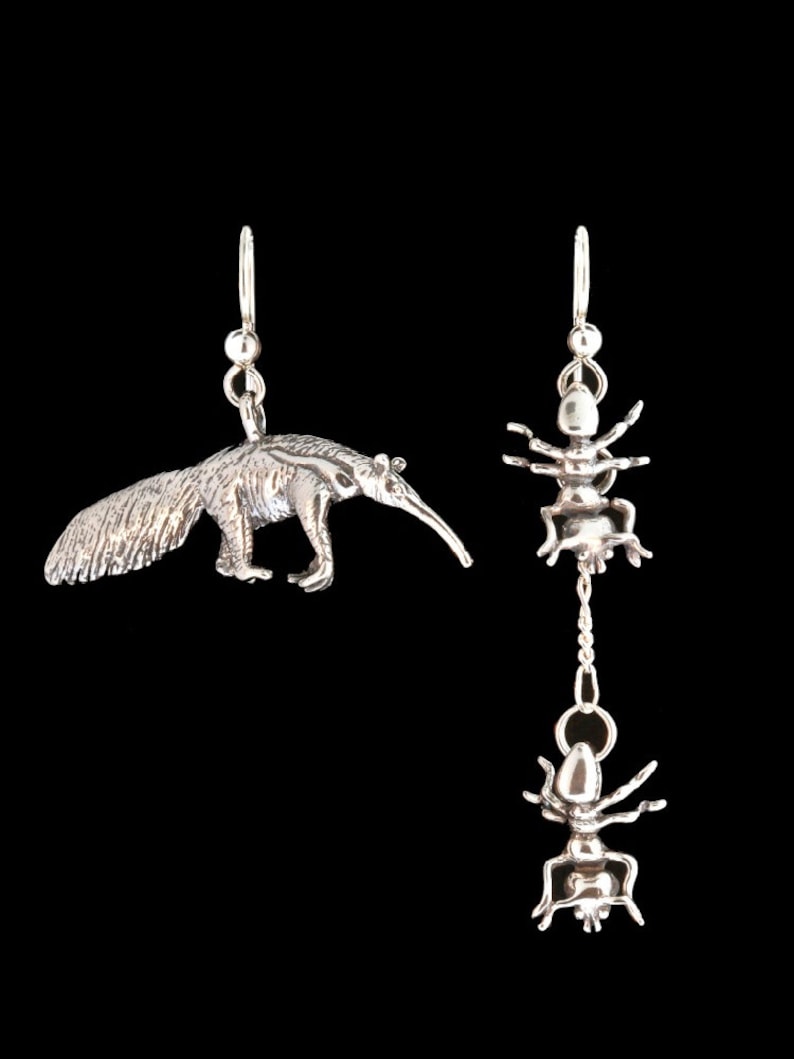 May include: A pair of silver earrings, one featuring an ant and the other an anteater. The ant earring has a dangling ant charm.