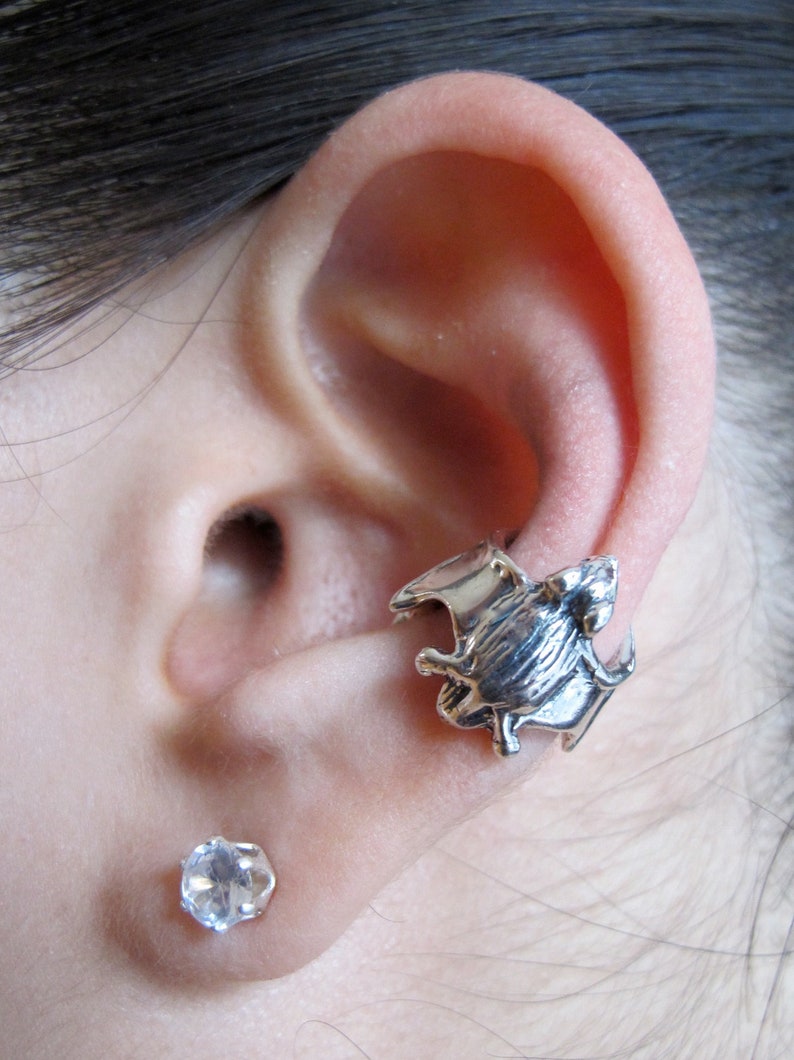 May include: Silver ear cuff in the shape of a bat with a clear crystal stud earring in the lower lobe.