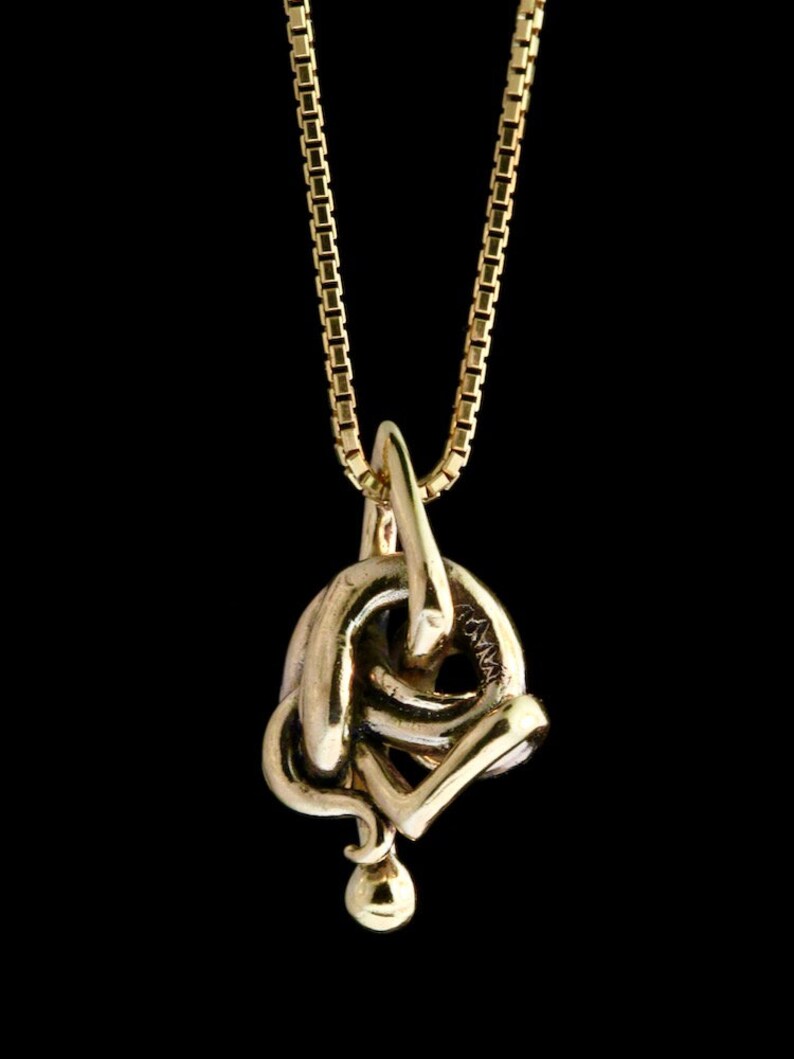 May include: A gold chain necklace with a gold pendant in the shape of a knot.