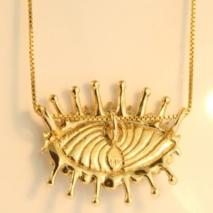 May include: A gold eye pendant necklace with a 14K stamp on the back. The eye is detailed with a swirling pattern and has a dripping effect around the edges.