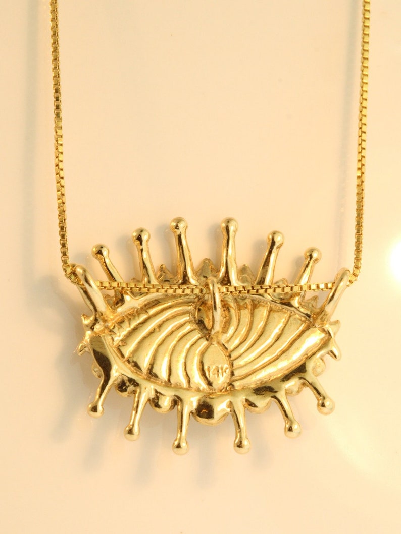 May include: A gold eye pendant necklace with a 14K stamp on the back. The eye is detailed with a swirling pattern and has a dripping effect around the edges.
