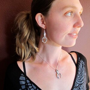 Op de afbeelding: Een vrouw draagt een zwart-grijs gem&ecirc;leerd shirt met een zilveren drakenhangerketting en bijpassende zilveren drakenoorbellen.