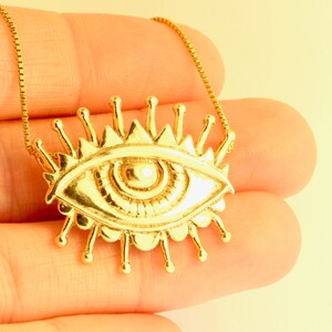 May include: A gold necklace with a large eye pendant. The eye is surrounded by a circle of rays.