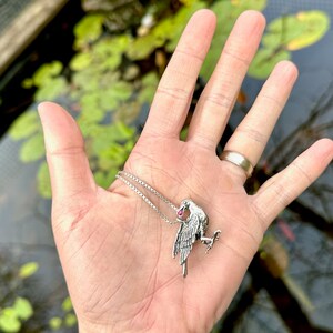 May include: A silver chain necklace with a detailed silver bird pendant featuring a pink gemstone in its beak.