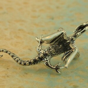 May include: A detailed silver dragon figurine with outstretched wings and a long tail. The dragon has textured scales and is posed as if in flight. The figurine is set against a light-colored background.