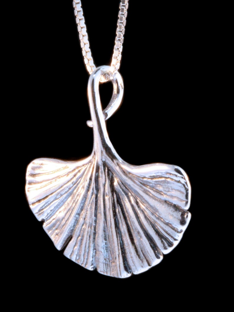 May include: A silver pendant necklace featuring a detailed ginkgo leaf design. The pendant is attached to a silver chain.