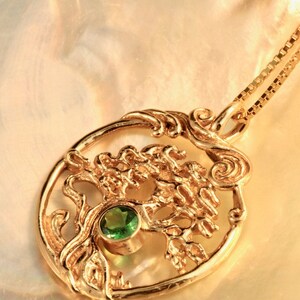 May include: A gold pendant necklace featuring a detailed tree of life design with a green gemstone at the center. The pendant is on a gold chain.