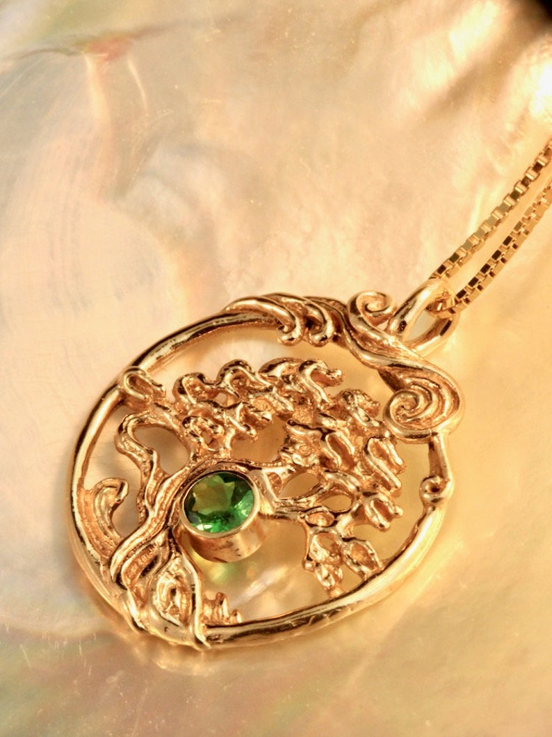 May include: A gold pendant necklace featuring a detailed tree of life design with a green gemstone at the center. The pendant is on a gold chain.