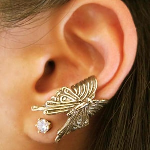 May include: A silver butterfly ear cuff with a clear crystal stud earring. The ear cuff is designed to sit on the upper part of the ear.