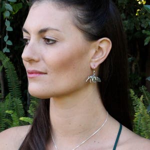 May include: A woman wearing a green tank top and a silver necklace with a beetle pendant. She is also wearing silver earrings with a beetle design.
