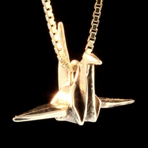 May include: A gold origami crane pendant necklace. The crane is a symbol of peace and good luck.
