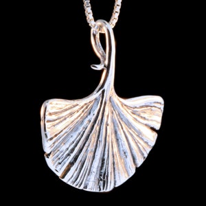 May include: A silver pendant necklace featuring a detailed ginkgo leaf design. The pendant is attached to a silver chain.