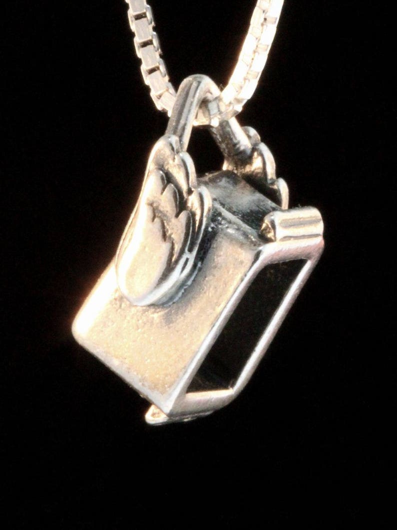 May include: A silver charm necklace pendant shaped like a small, open-top box with a hinged lid. The box has a detailed design and a smooth, polished finish.