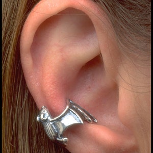 May include: A silver bat ear cuff with a small, clear crystal stud earring in the lower lobe of the ear.
