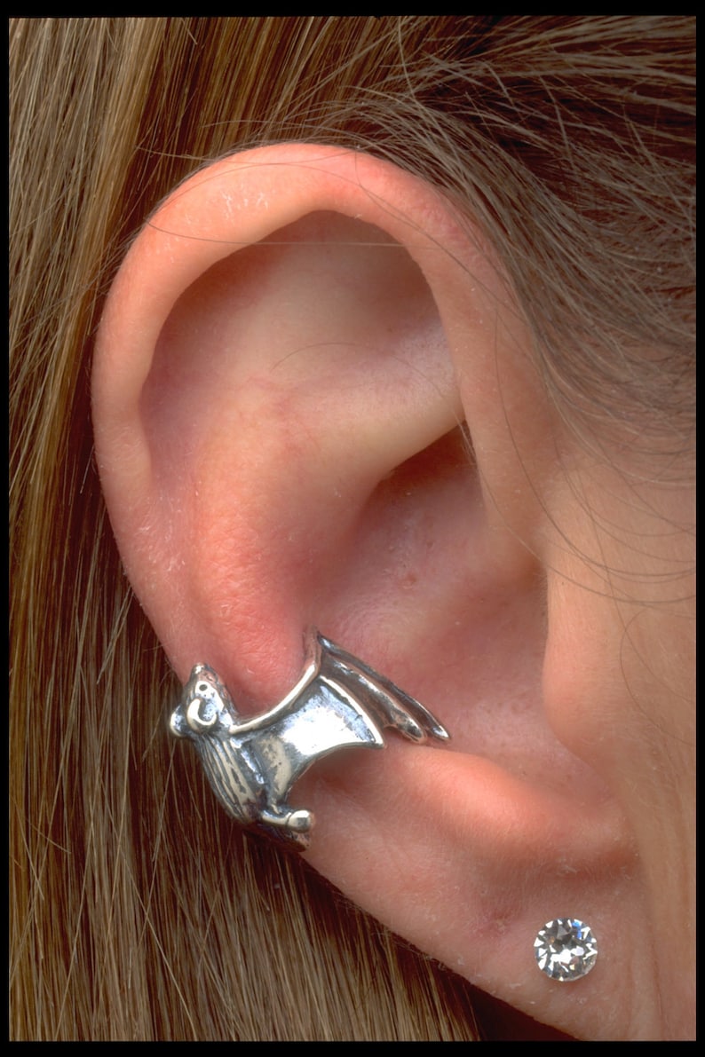 May include: A silver bat ear cuff with a small, clear crystal stud earring in the lower lobe of the ear.