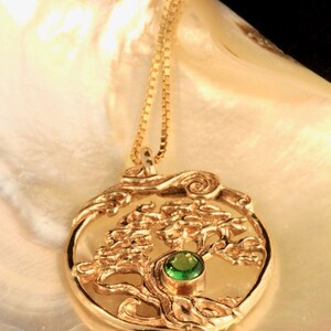 May include: A gold necklace with a pendant featuring a detailed tree of life design with a green gemstone in the center.