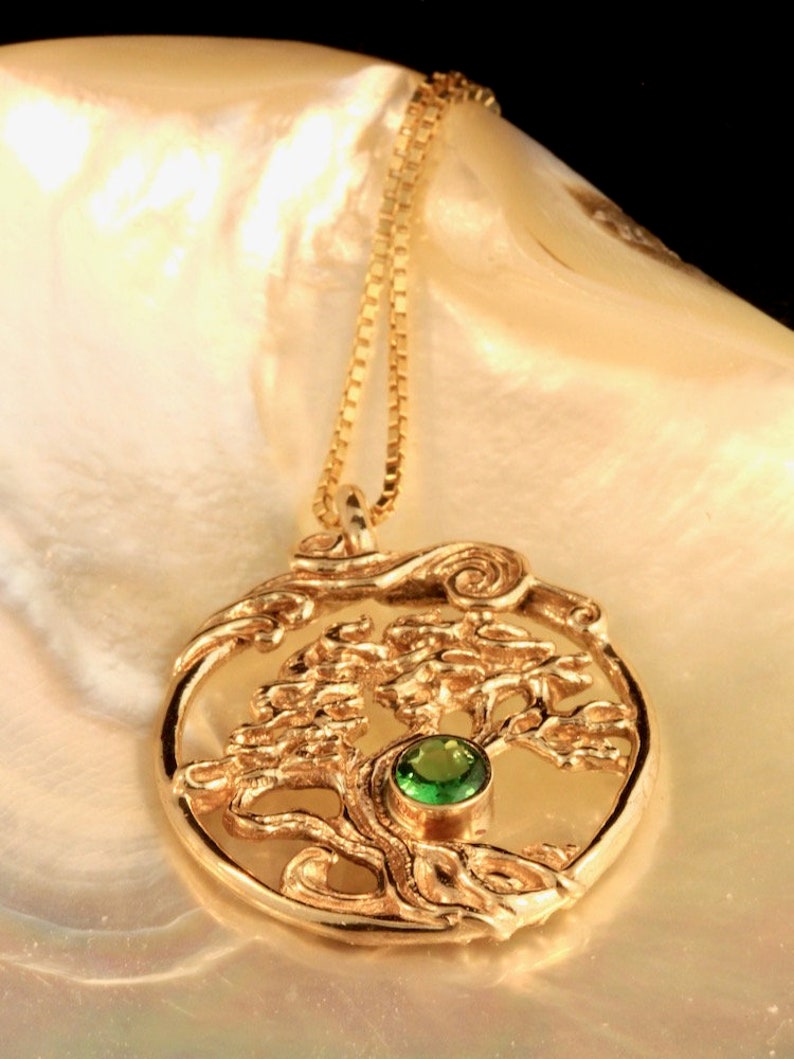 May include: A gold necklace with a pendant featuring a detailed tree of life design with a green gemstone in the center.