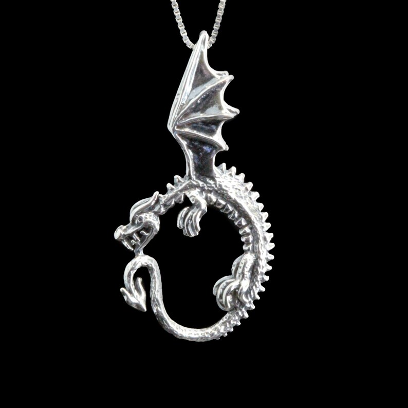 Op de afbeelding: Zilveren ketting met hanger met een gedetailleerd drakenontwerp met uitgespreide vleugels en een staart die om zijn lichaam is gekruld.