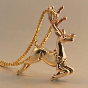 May include: A gold reindeer pendant with a red jewel on its nose, hanging from a gold chain.