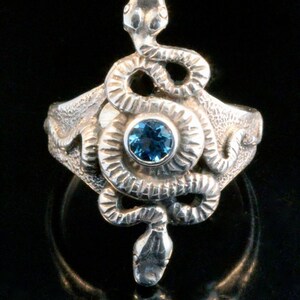 May include: A silver ring featuring a detailed snake design with a blue gemstone in the centre.